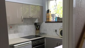 A compact kitchen with white cabinets, a dishwasher, an oven, and a sink. There is a window with a view of greenery outside. - PLAN YOUR ISLAND ESCAPE TO THE BEAUTIFUL SCOTTISH ISLE OF CUMBRAE (Millport)