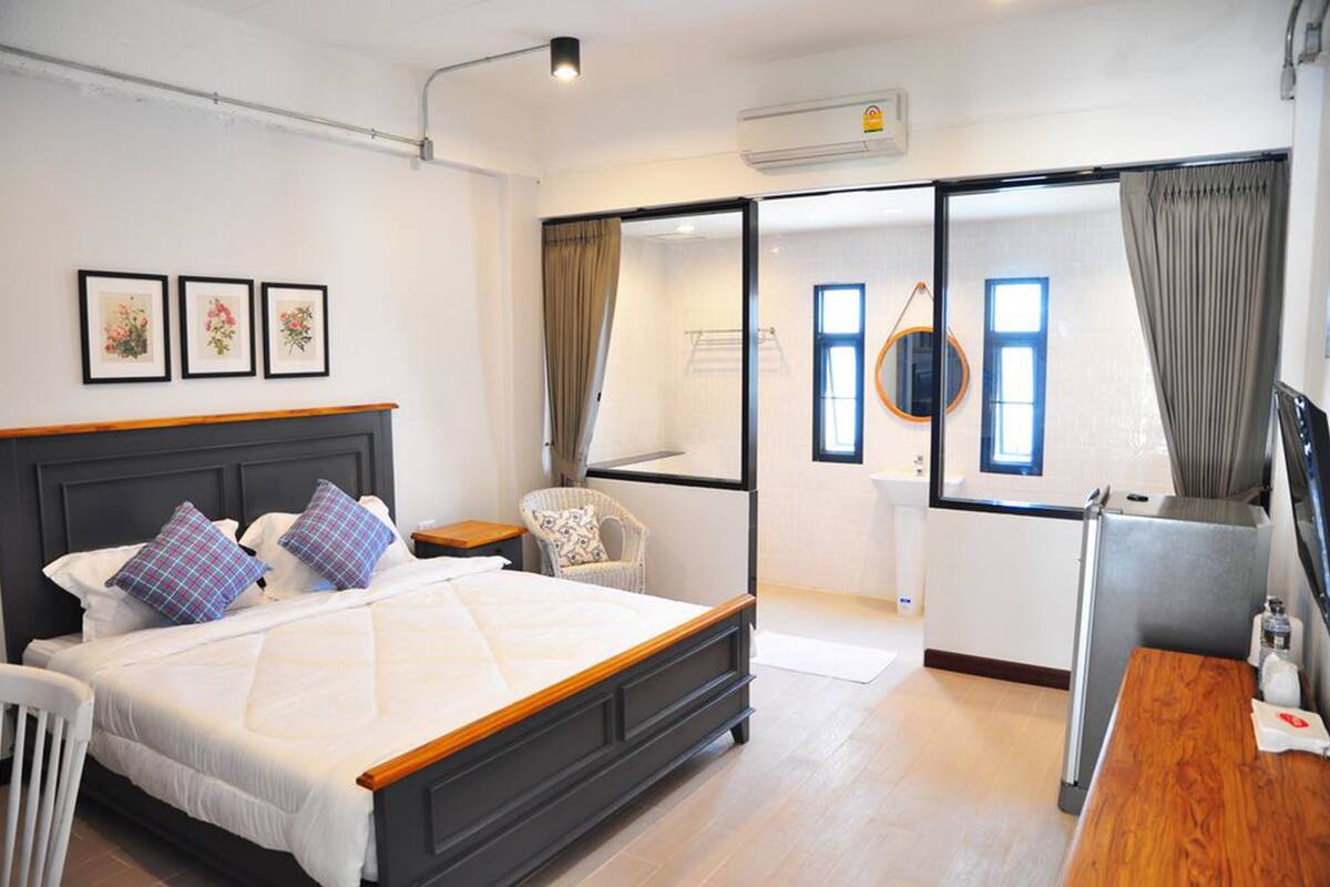 Ein modernes Hotelzimmer mit einem großen Bett, einem Schreibtisch, einem Stuhl und Blick auf die Stadt durch eine Glastür.