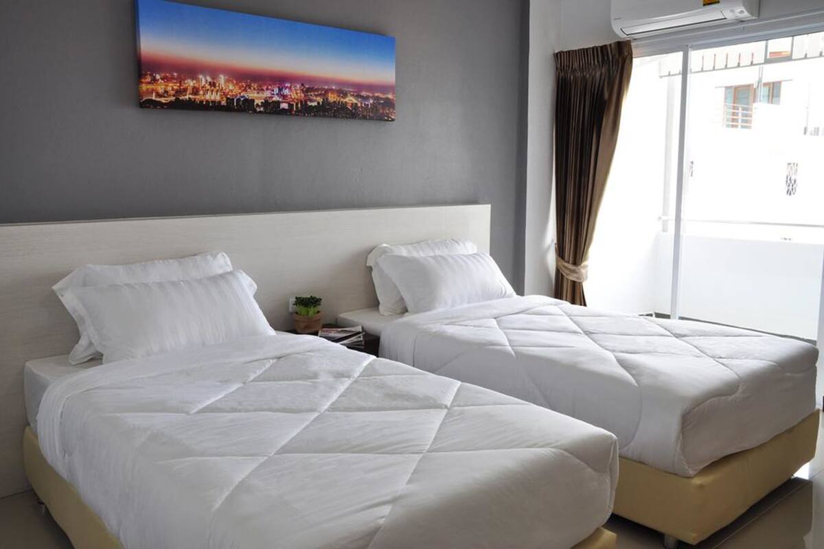 Ein Hotelzimmer mit zwei Betten, einem Stadtbild an der Wand und einem Fenster mit Vorhängen.