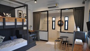 A compact hotel room with a bunk bed, a small kitchenette, a dining area with stools, and a sliding glass door leading to a bathroom. - C Room (Chomchan) at Airport (Chiang Mai)