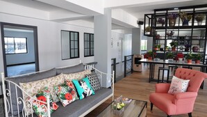 A spacious living area with a sofa, armchair, and a coffee table. There is a black shelving unit with plants and decorative items. - C Room (Chomchan) at Airport (Chiang Mai)