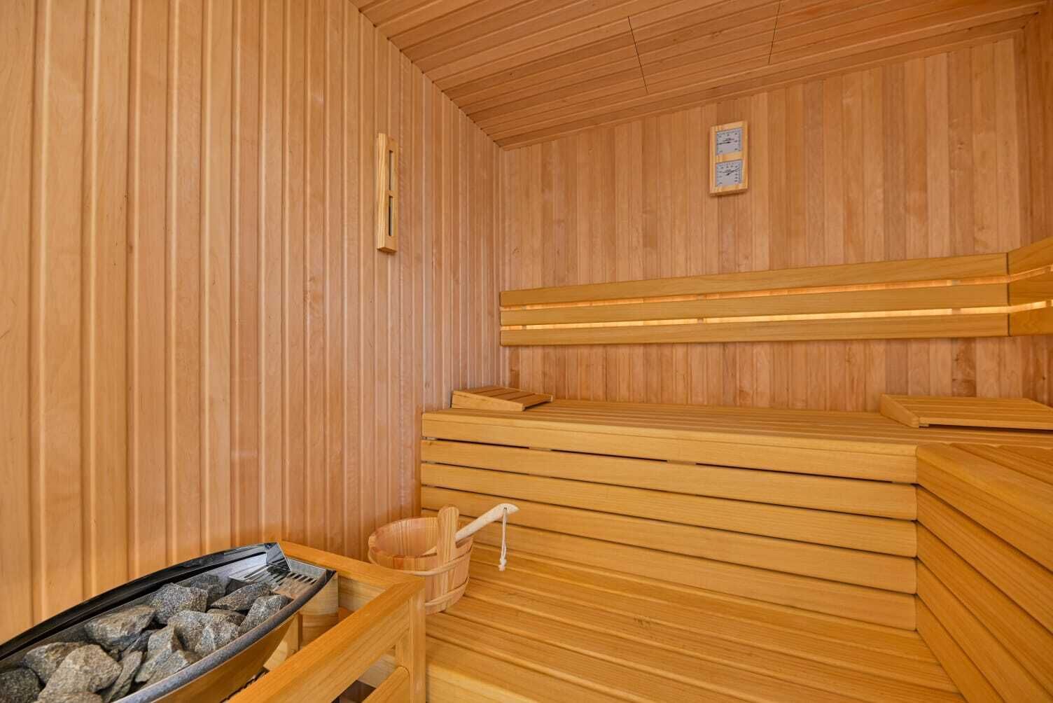 A wooden sauna with benches, a stone basin, and a wooden bucket.