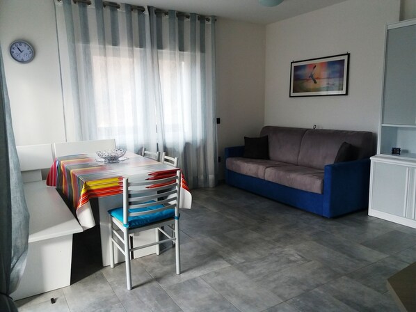 A living room with a dining table, chairs, a sofa, and a painting on the wall.