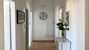 A hallway with a clock on the wall, a vase of flowers, and a white console table. - Modern and cozy Italian experience (Mestre)