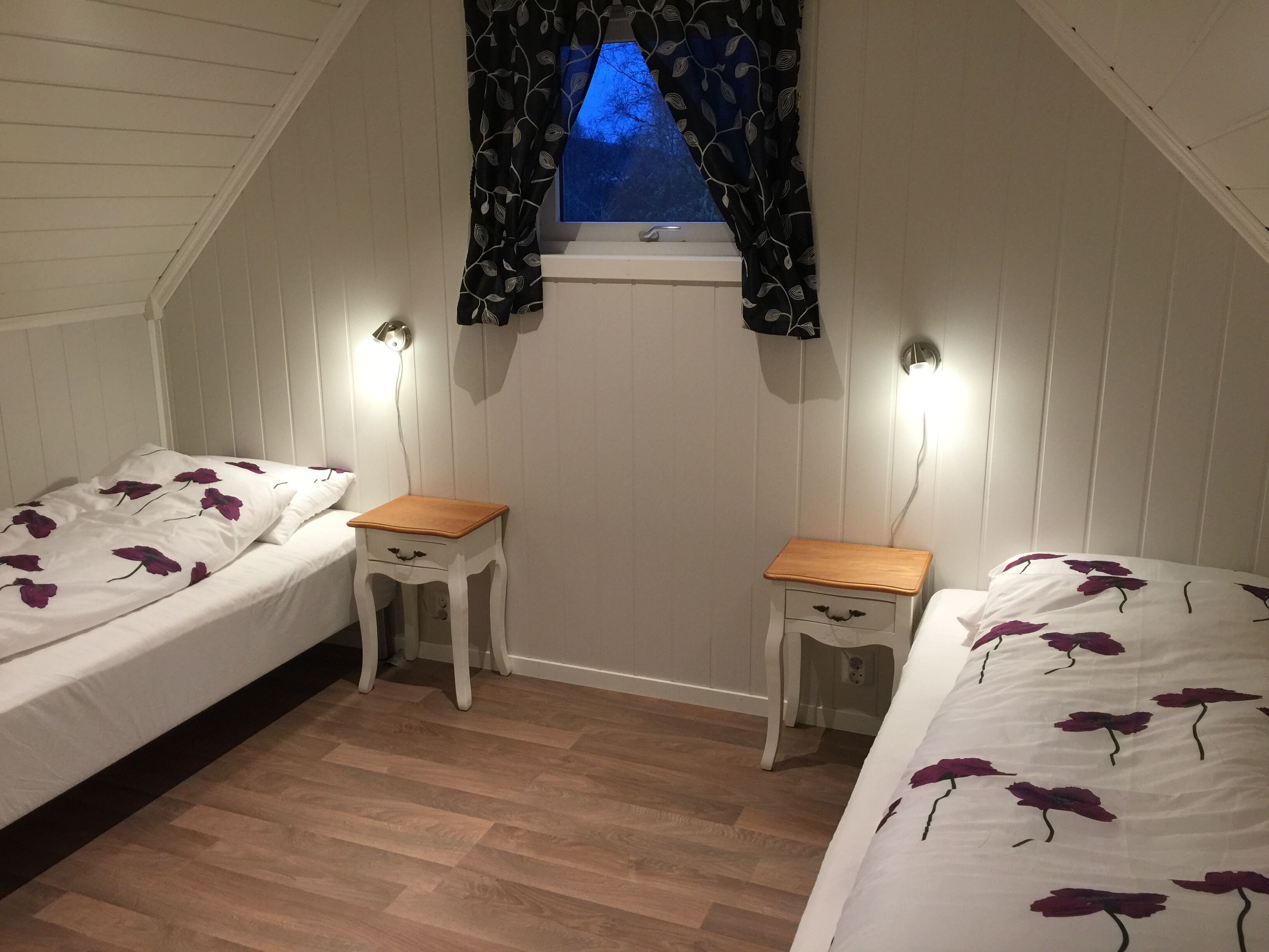 Quarto com duas camas de solteiro, uma janela pequena com vista e chão de madeira.