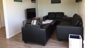 Een moderne woonkamer met een hoekbank, een flatscreen televisie en twee schilderijen aan de muur.