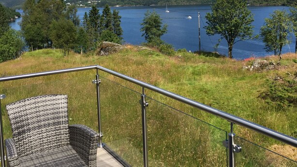Een balkon met rieten meubilair, met uitzicht op een meer en heuvels.