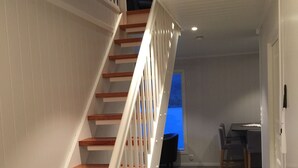 Een trap met houten treden en witte leuningen die leidt naar een kamer met een eettafel en stoelen.