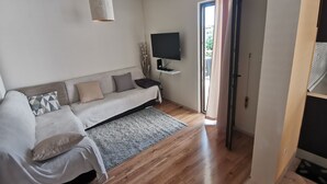 A modern bedroom with a sofa bed, a flat-screen TV, and a ceiling light. - Family apartment in Stobrec (Stobrec)