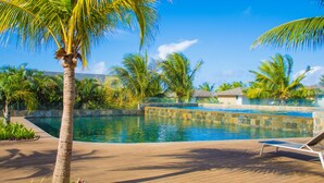 A pool area with a wooden deck, palm trees, and a clear blue sky.