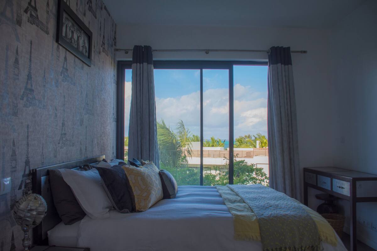 A bedroom with a large bed, a view of the outdoors, and a window with curtains.