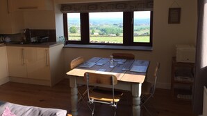 A kitchen with a large window, wooden table, and chairs. - Law Brook Farm cottage with stunning views . (Hudderfield)