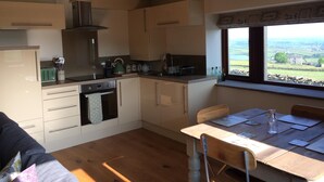 A kitchen with wooden cabinets, a stove, and a window overlooking a rural landscape. - Law Brook Farm cottage with stunning views . (Hudderfield)