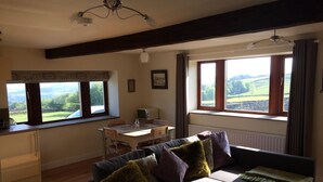 A cozy living room with a sofa, a dining table, and a view of the countryside through large windows. - Law Brook Farm cottage with stunning views . (Hudderfield)