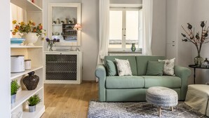 Een woonkamer met een groene bank, een kamerbreed tapijt en een raam met witte gordijnen.