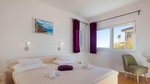 A bedroom with a large bed, two bedside tables, a chair, a painting on the wall, and a window with curtains.