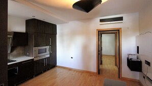 Una cocina moderna con armarios oscuros, electrodomésticos de acero inoxidable, piso de madera y una lámpara empotrada.
