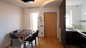 Una cocina compacta con un lavamanos, una zona de comedor con mesa y sillas, y una puerta que da a otra habitación.