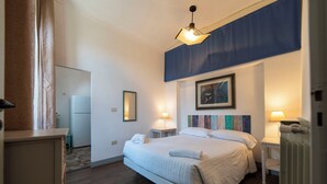 A hotel room with a bed, bedside tables, a radiator, a window with curtains, a wall-mounted painting, and a small kitchenette. - Large apartment at Residece Ca of NI - Finalborgo (Finale Ligure)