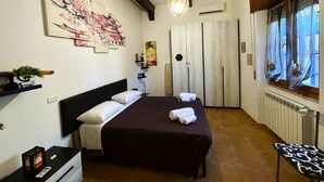 Habitación de hotel con cama, escritorio, silla, ventana con cortinas, un cuadro en la pared y lámpara colgante.