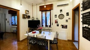 Un comedor con mesa, sillas y televisor. Se observan adornos en la pared y un ventanal con cortinas.