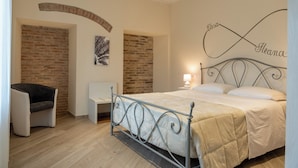 A bedroom with a bed, a chair, a small table, and a brick wall.