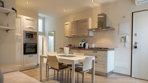 A modern kitchen with built-in appliances, a dining area with a white table and chairs, and a light-colored floor.