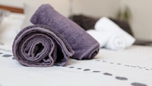 Ein ordentlich gefaltetes Set an Handtüchern auf einem Bett mit einer grau-weißen Bettdecke.