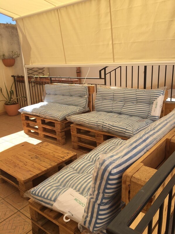 A wooden outdoor seating area with striped cushions, a covered section, and a potted plant.