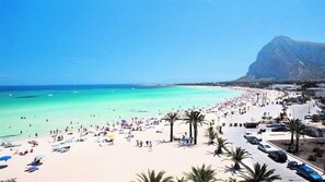 A beach with clear turquoise waters, palm trees, and a mountain in the background.