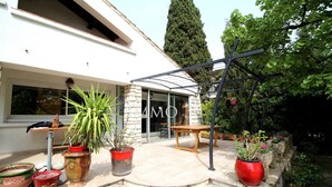 Una casa moderna con un patio que cuenta con plantas en macetas, una mesa de madera y un muro de piedra.