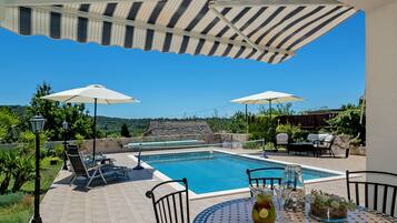 Relax by the pool surrounded by lush greenery and distant hills.