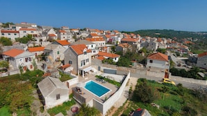 A coastal village with stone buildings, a swimming pool, and a clear blue sky.