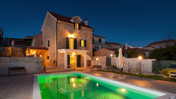 A stone house with a swimming pool, outdoor seating, and a staircase leading to the entrance.