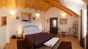 A bedroom with a bed, bedside tables, a chair, a small table, a shelf with books, and a painting on the wall.