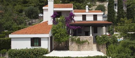 A two-story house with a tiled roof, white walls, and a stone foundation.