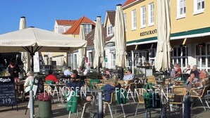 Un café avec des tables en terrasse, un restaurant en arrière-plan et un ciel bleu dégagé.