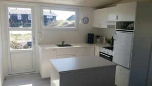 Une cuisine moderne avec des meubles blancs, un four encastré, un réfrigérateur et une fenêtre donnant sur un espace verdoyant.