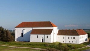 Un grand bâtiment blanc coiffé d’un toit rouge, probablement un hôtel ou un bâtiment public, situé dans une zone rurale, avec de vastes champs à perte de vue et un ciel dégagé.