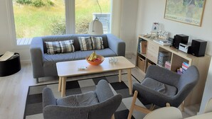 Un salon moderne avec un canapé gris, une table basse en bois et un fauteuil gris. On y trouve une bibliothèque remplie de livres et un tableau encadré accroché au mur.