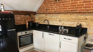 Una cocina compacta con armarios blancos, encimera negra, horno integrado y pared de ladrillo.