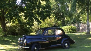 Un coche clásico negro estacionado sobre un césped con árboles al fondo.