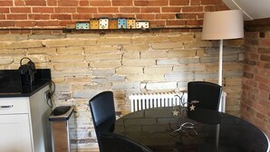 Una cocina compacta con pared de ladrillo, una mesa de comedor con sillas, una cafetera y un radiador.
