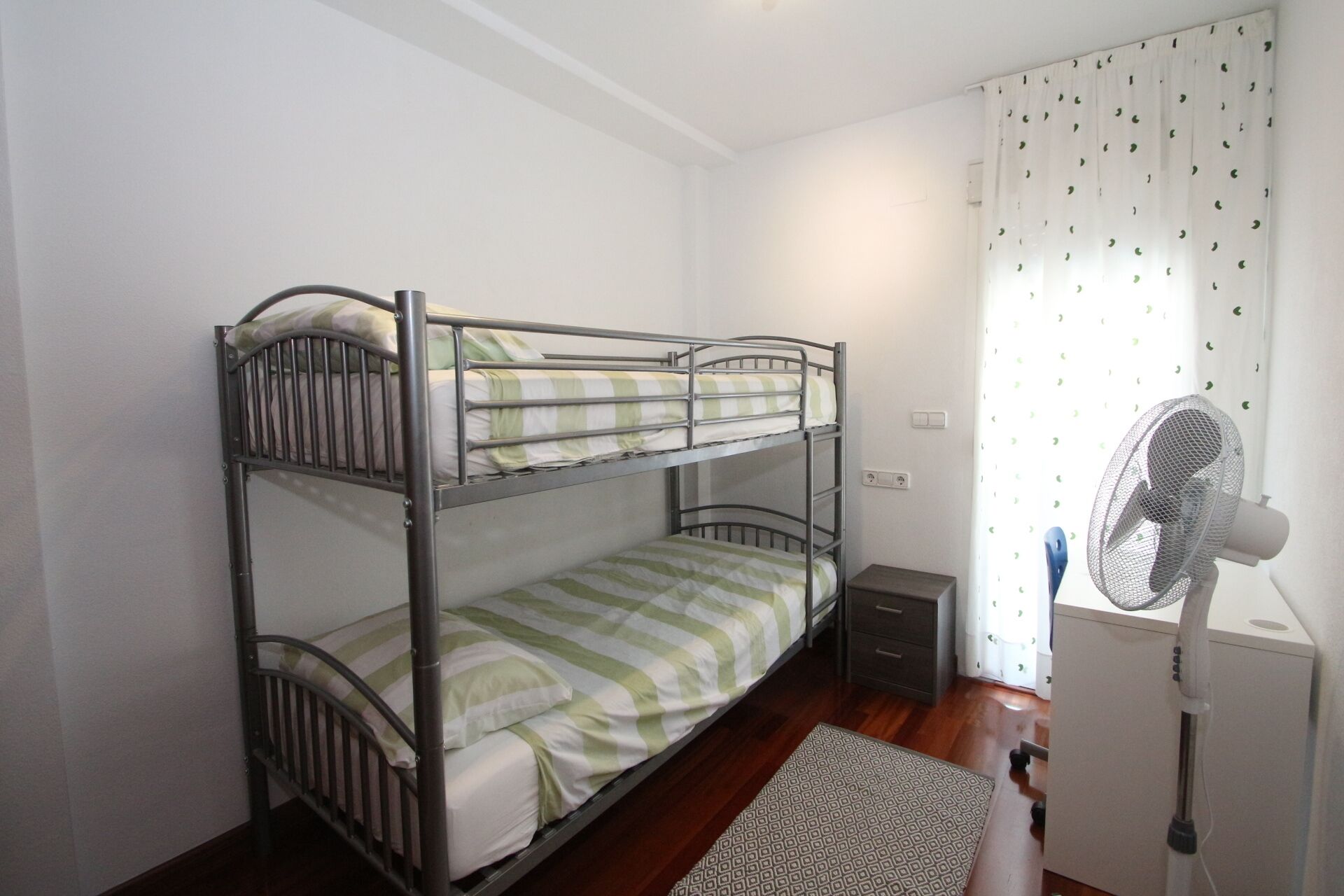A bunk bed room with a desk and a standing fan.