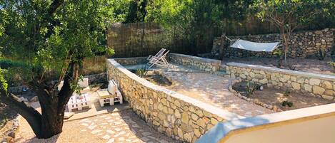 Un espacio al aire libre con paredes de piedra, una piscina, sillones de descanso y una hamaca.