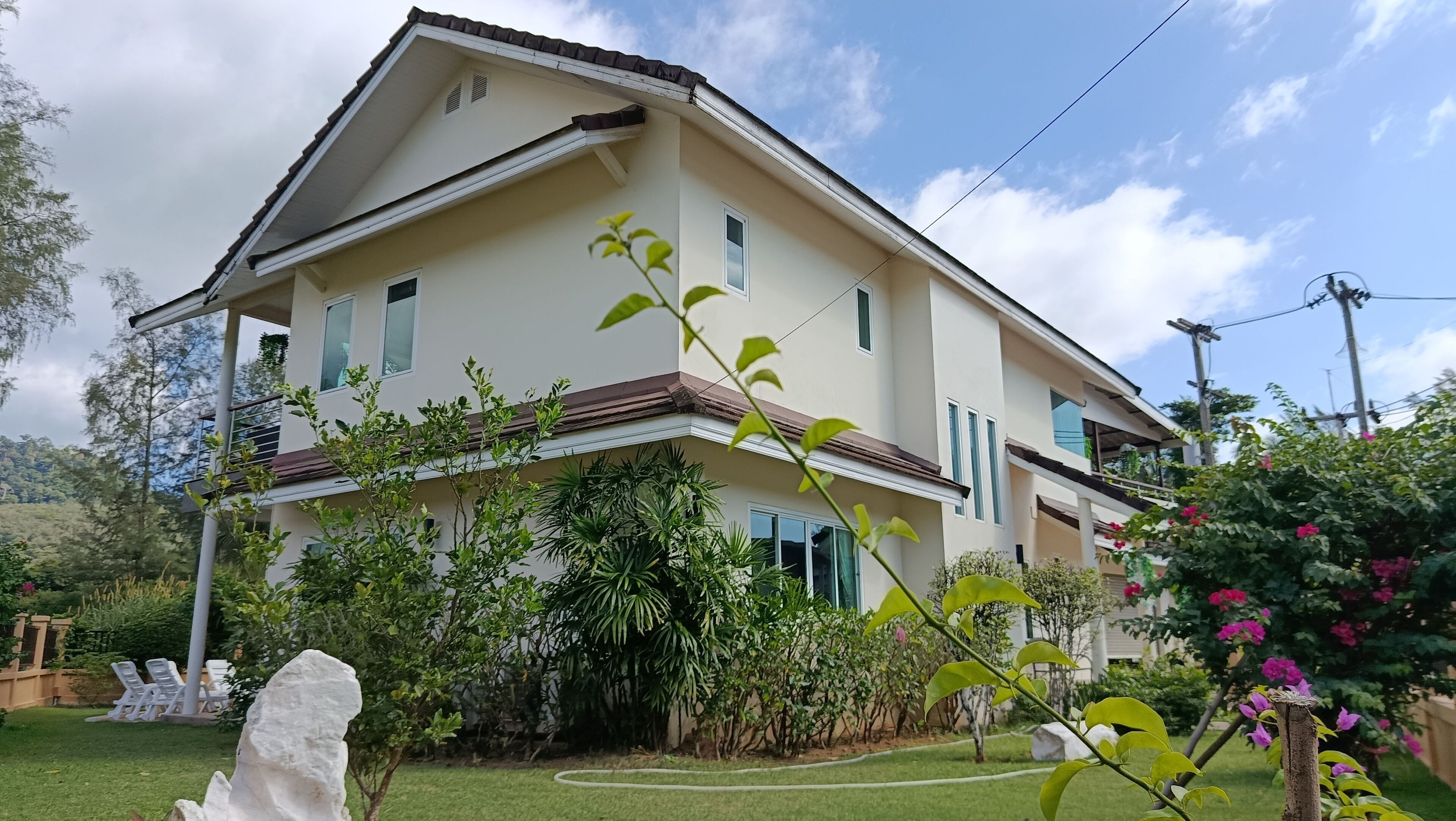 A two-story house with a balcony, surrounded by lush greenery and a well-maintained lawn.