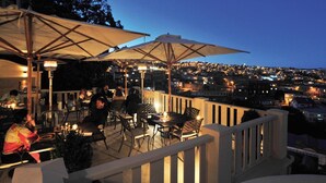 An outdoor dining area with tables and chairs, umbrellas, and a city view at dusk. - Sun-Drenched, Sea-View Apartment with Giant Patio, Private Garden and Garage (Fuengirola)