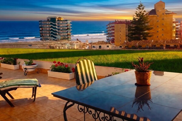 A terrace with a table, chairs, and potted plants, overlooking a beach and buildings. - Sun-Drenched, Sea-View Apartment with Giant Patio, Private Garden and Garage (Fuengirola)