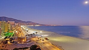 Eine Küstenstadt bei Nacht mit Strand, Gebäuden und einer Kreisverkehrsstraße.