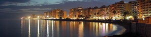 A waterfront cityscape with illuminated buildings reflecting on the calm water. - Sun-Drenched, Sea-View Apartment with Giant Patio, Private Garden and Garage (Fuengirola)